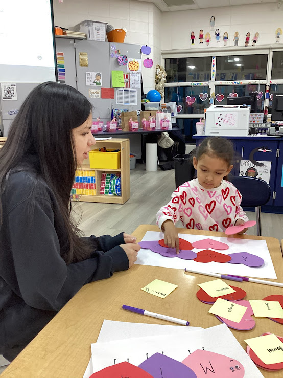 During Valentine's Day activities, Lancer Preschooler Kailani works on creating a lovebug craft by spelling out her name. Nicole Rosero (LP '26) guides her with the project.