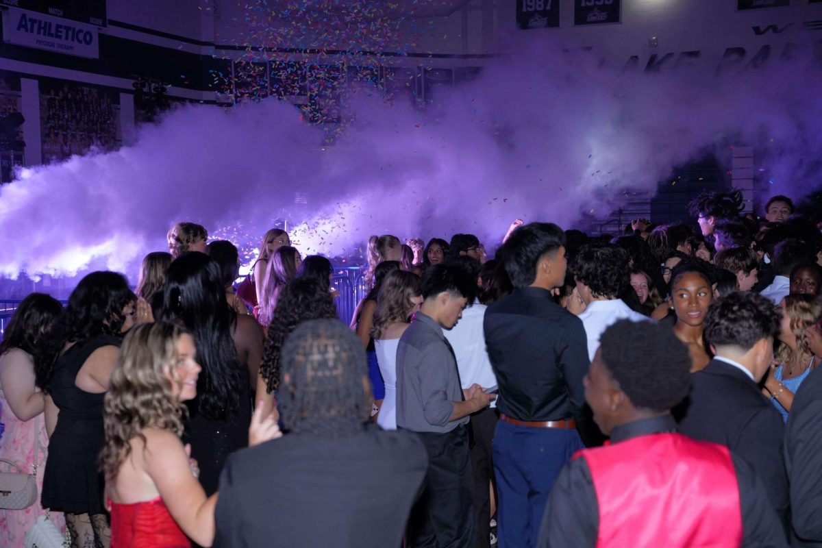Students gather as smoke and confetti are released into the crowd in the gym at the homecoming dance.